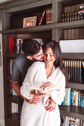 man-loving-her-wife-holding-open-book-front-bookshelf
