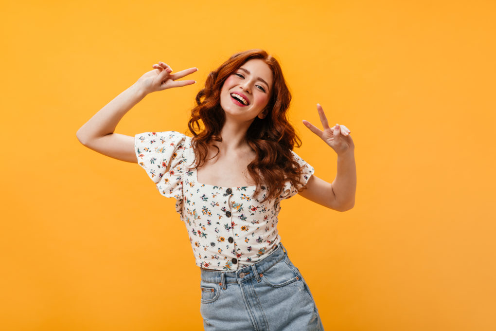 Portrait of curly girl in blouse and denim skirt showing peace sign