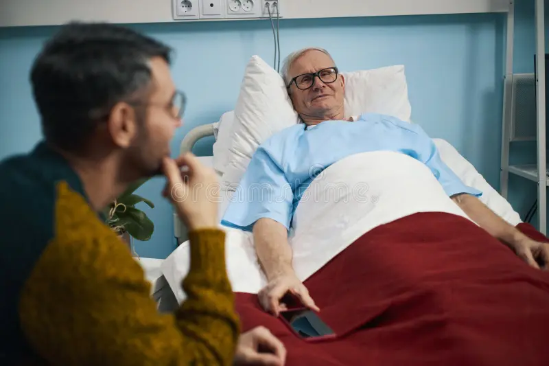 sick-senior-man-lying-hospital-bed-talking-to-his-son-visit-369318764